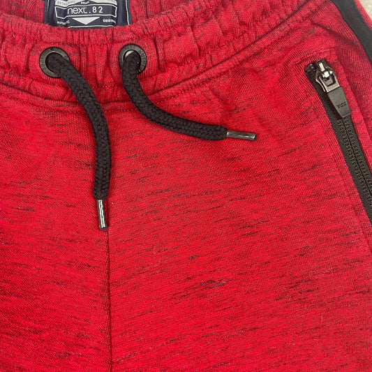 Rote Kinder-Sweatshorts mit schwarzen Reißverschluss-Taschen und seitlichen Streifen – detail