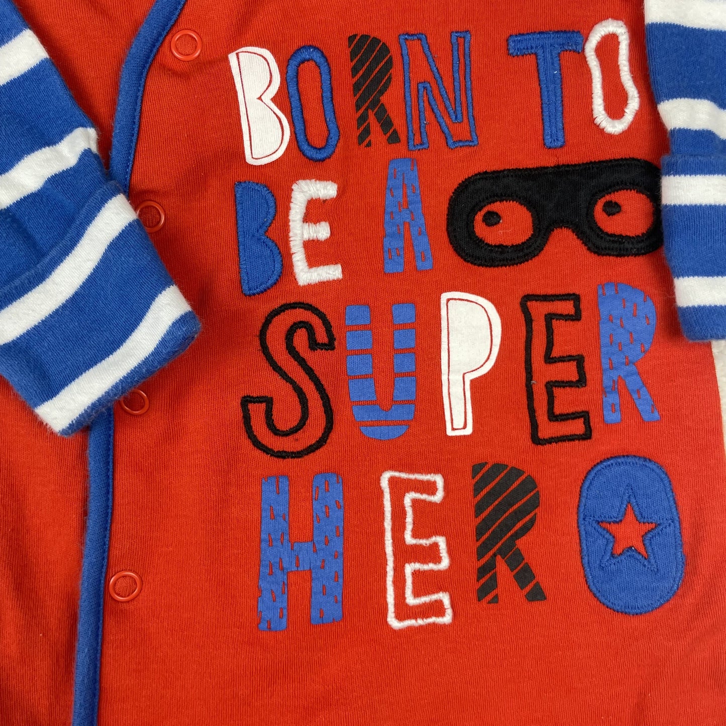 Roter Baby-Schlafanzug von Nutmeg mit blau-weiß gestreiften Ärmeln und Superhelden-Print, Größe 0–3 Monate. – detail