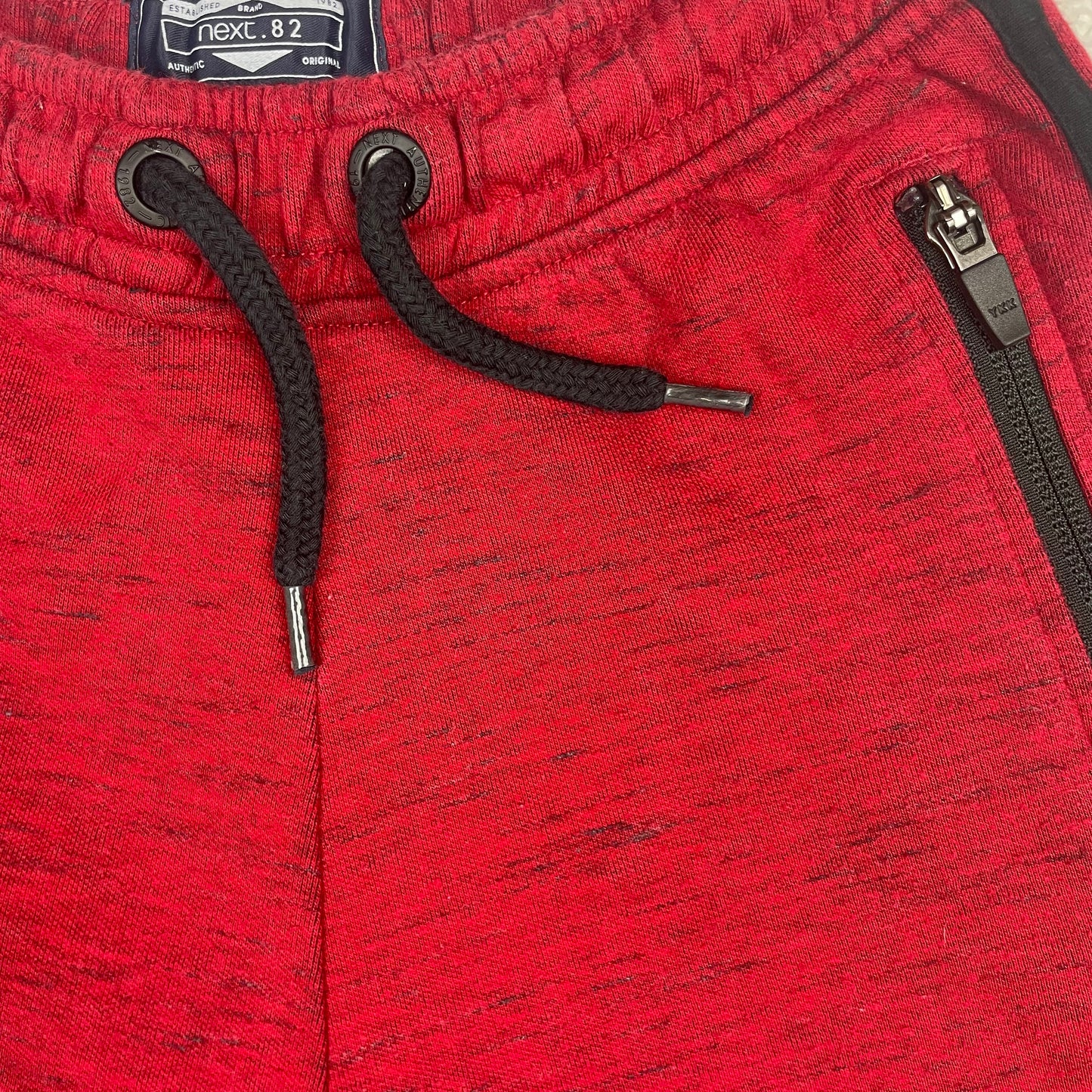 Rote Kinder-Sweatshorts mit schwarzen Reißverschluss-Taschen und seitlichen Streifen – detail