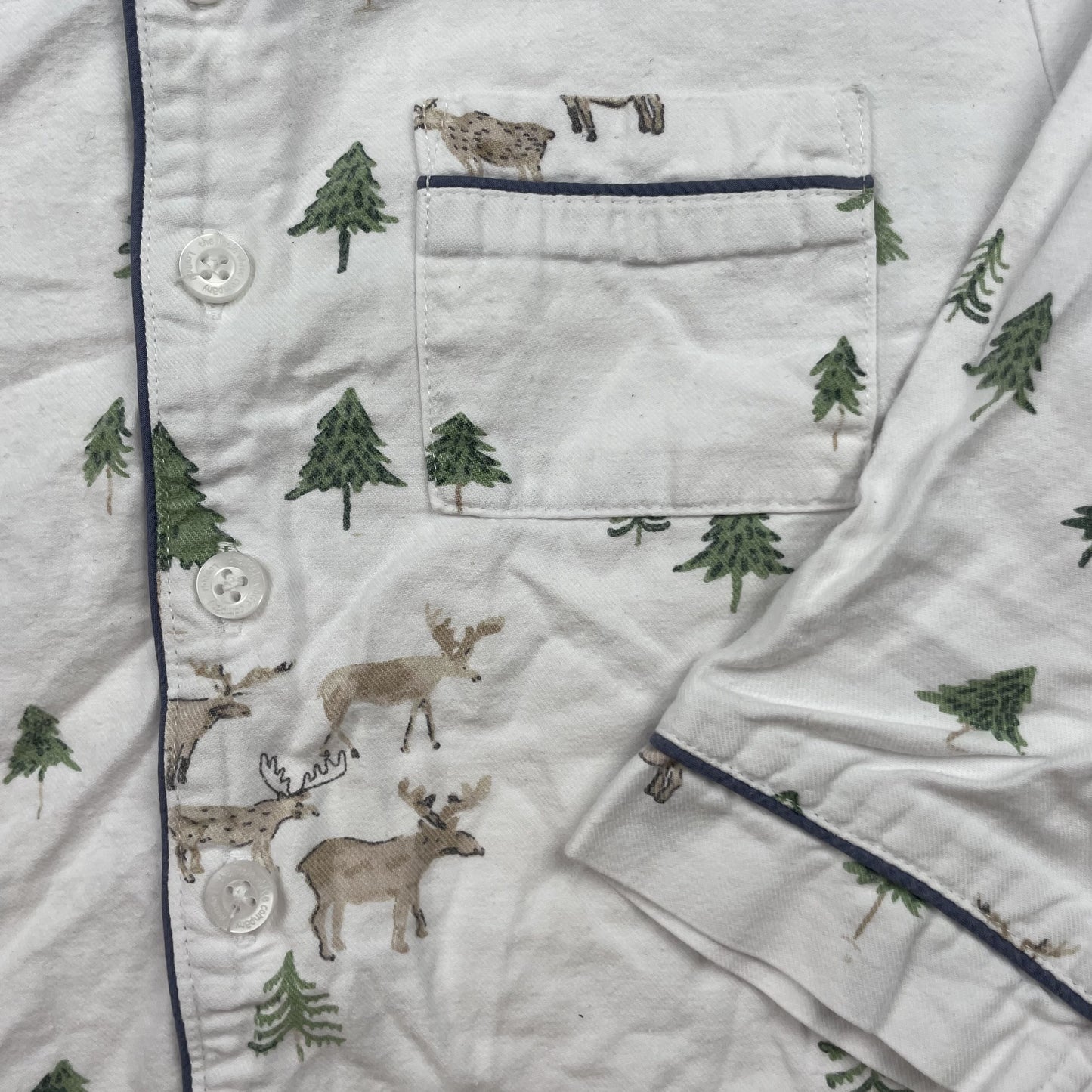 Weißes Schlafanzugoberteil mit Rentier- und Tannenmuster, lange Ärmel und dunkelblaue Paspeln – detail