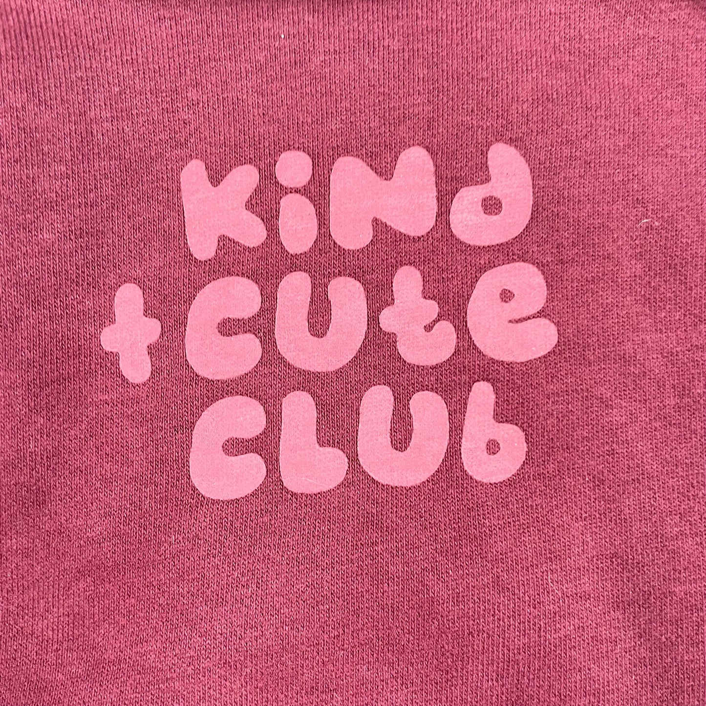 Bordeauxfarbener Pullover mit "Kind Cute Club" Aufdruck und Druckknöpfen an der Schulter. – detail