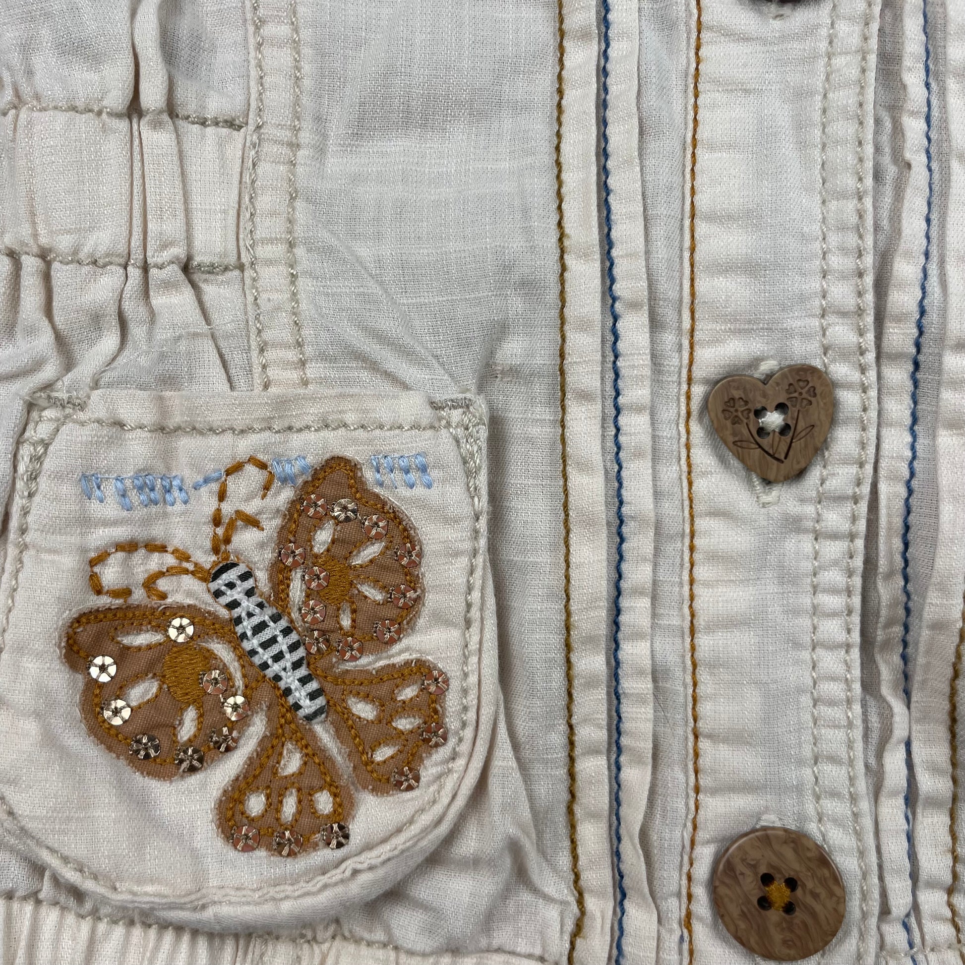 Beige Kapuzenjacke mit Schmetterlingsmotiven auf den Taschen – detail