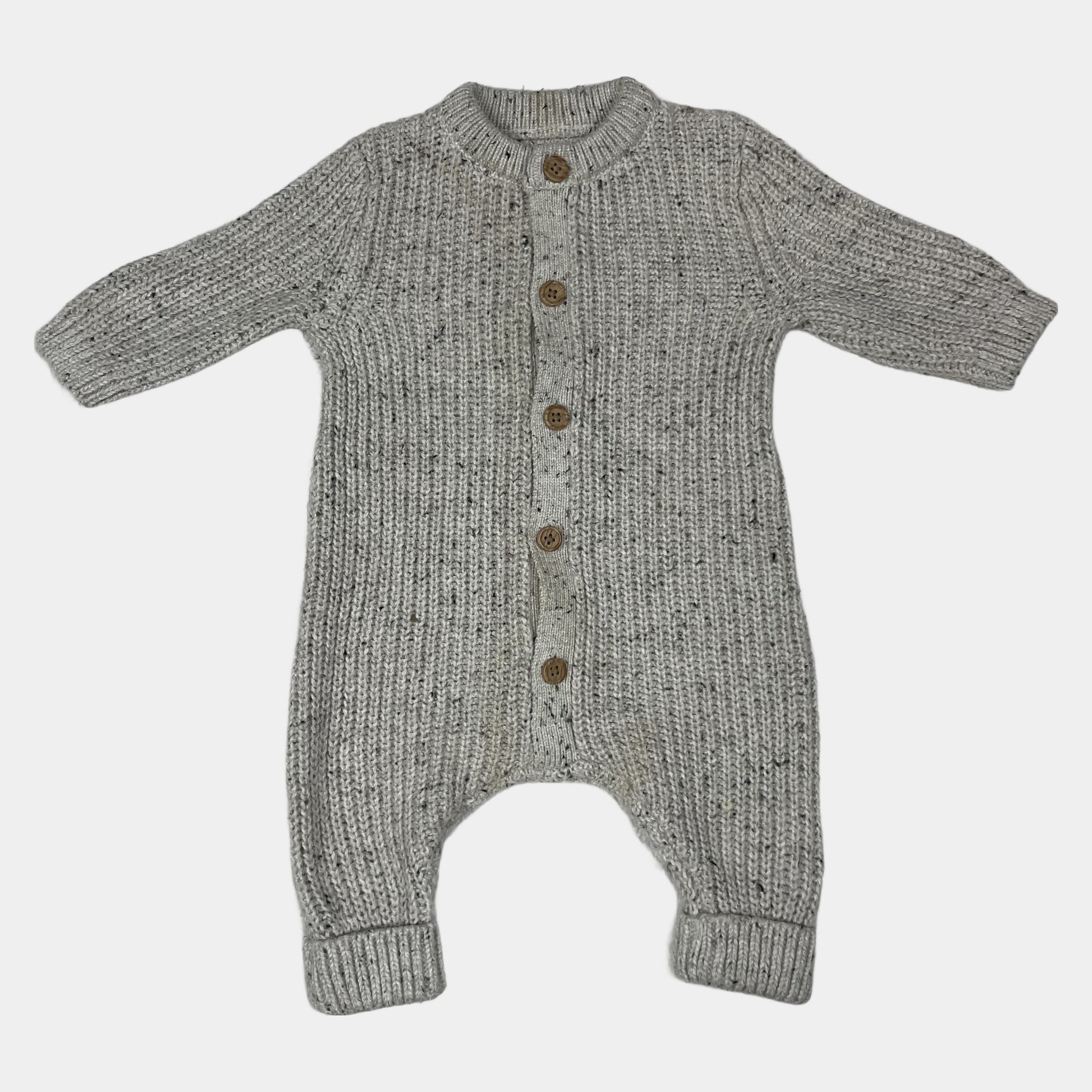 Grauer Overall aus Strick mit Holzknöpfen auf hellgrauer Unterlage – front