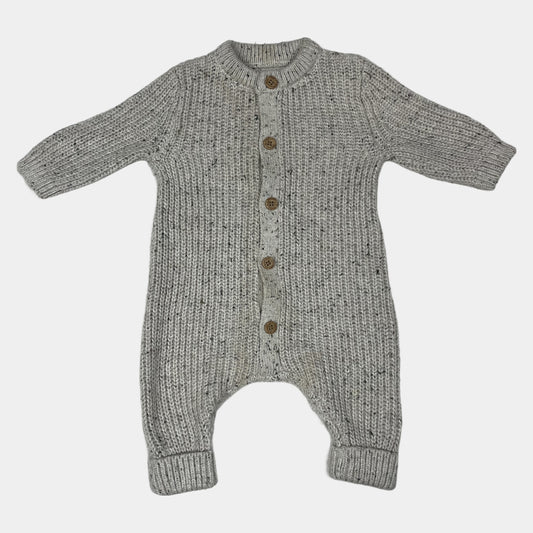 Grauer Overall aus Strick mit Holzknöpfen auf hellgrauer Unterlage – front