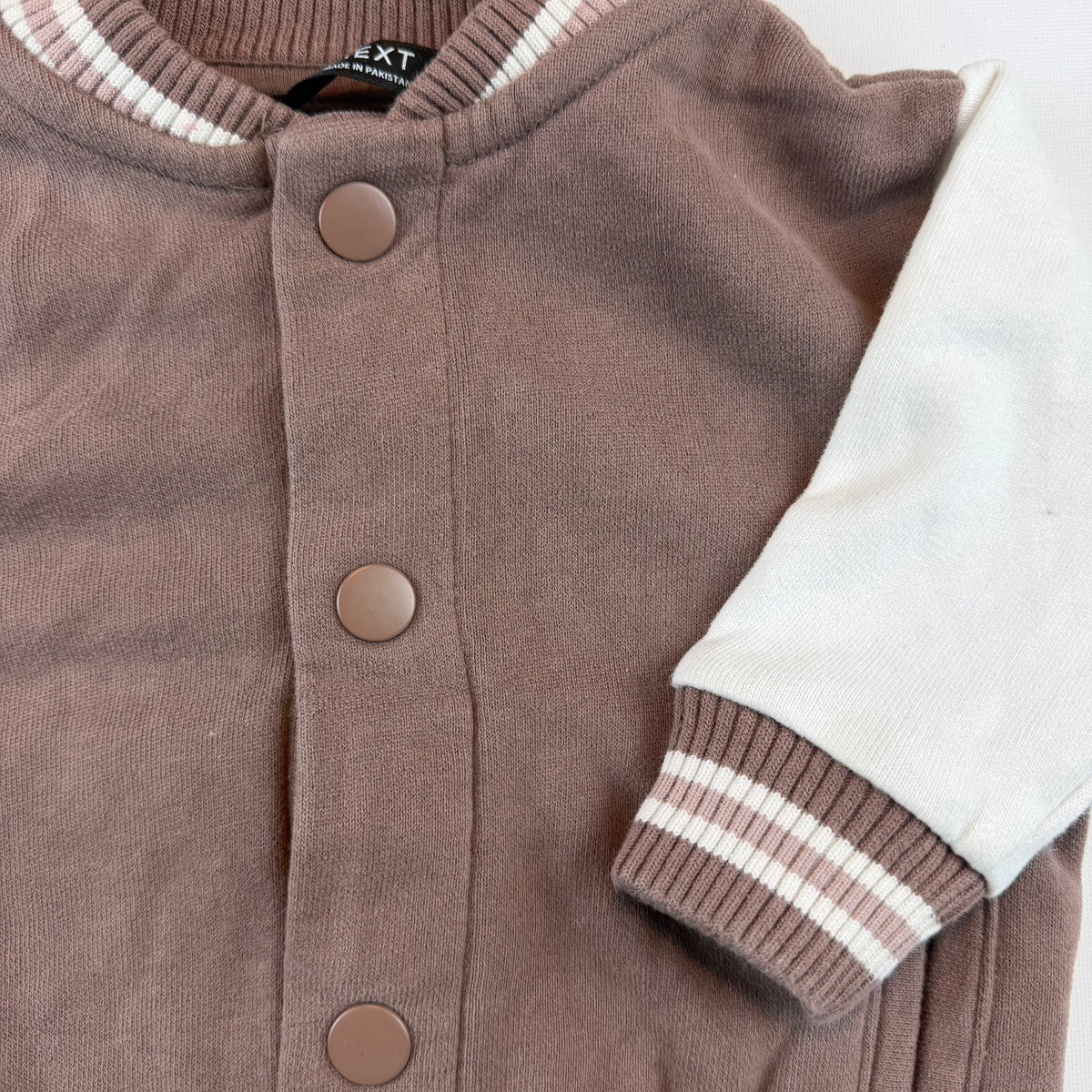 Braune Baby-Collegejacke mit weißen Ärmeln und Druckknöpfen – detail